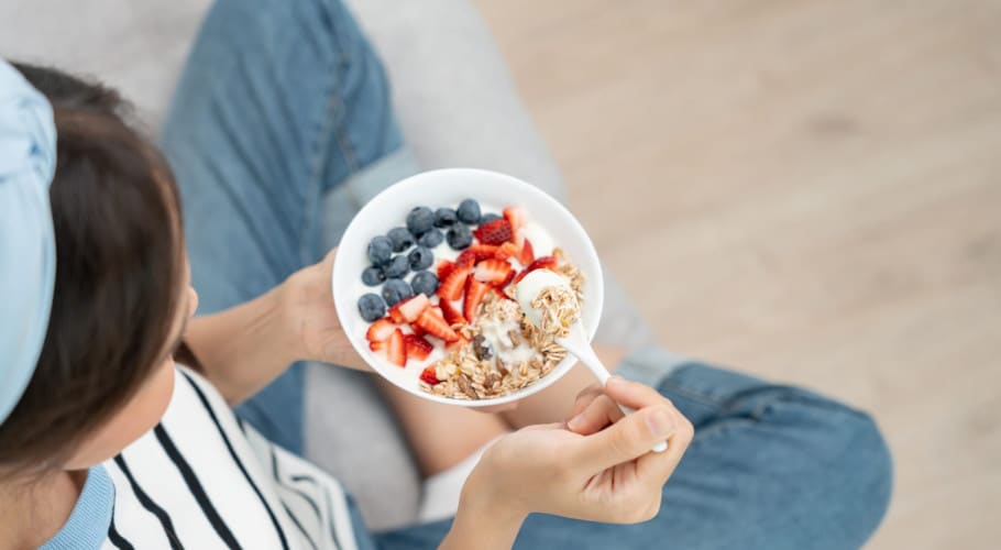 A woman holding a bowl of oats, strawberries, blueberries and milk, a healthy breakfast that's good for the gut.