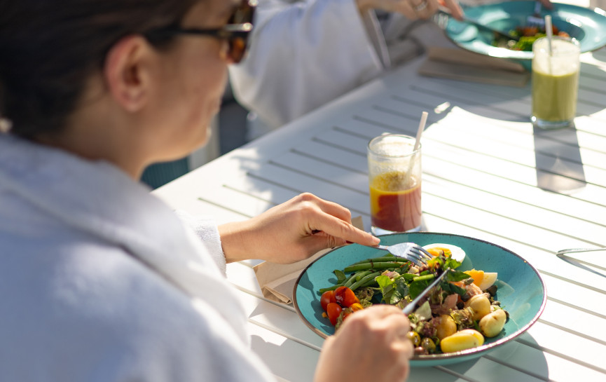 Guests in spa robes enjoy fresh, healthy salads and juices outdoors at Glass House Wellness Centre, seated at a white table in the sunshine.