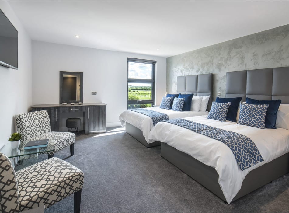 Two beds, with desk and chairs in room with view out of window