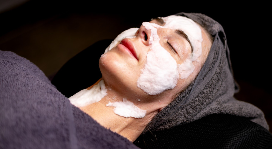 Guest enjoying a soothing facial at Glass House Wellness Retreat & Spa, with a creamy mask applied and hair wrapped in a towel, eyes closed in relaxation.