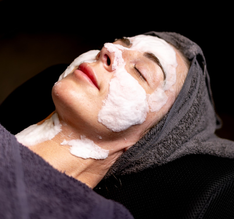 Guest enjoying a soothing facial at Glass House Wellness Retreat & Spa, with a creamy mask applied and hair wrapped in a towel, eyes closed in relaxation.