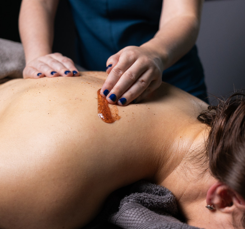 Body exfoliation treatment at Glass House Wellness Retreat & Spa, with therapist applying a natural scrub to a guest’s back on a massage table.