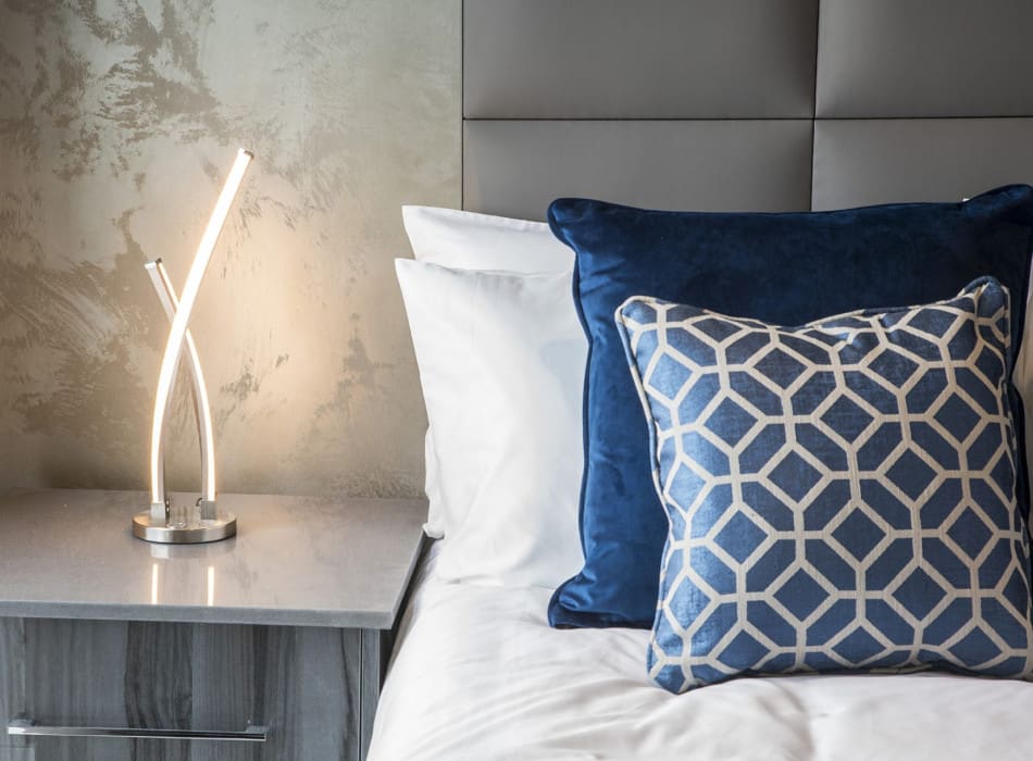 Lamp on beside table next to cushions on bed