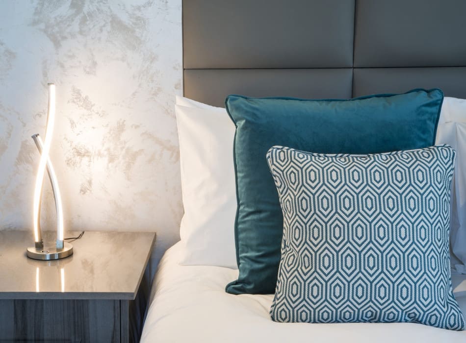 Lamp on bedside table next to cushions on bed