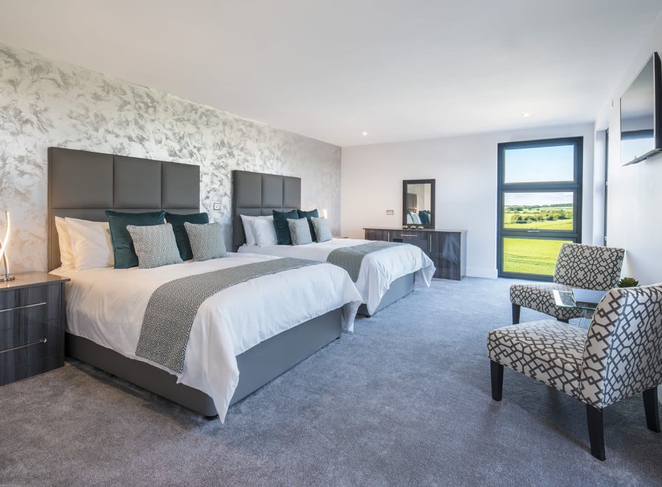 Two beds, desk and chairs in room with view from window