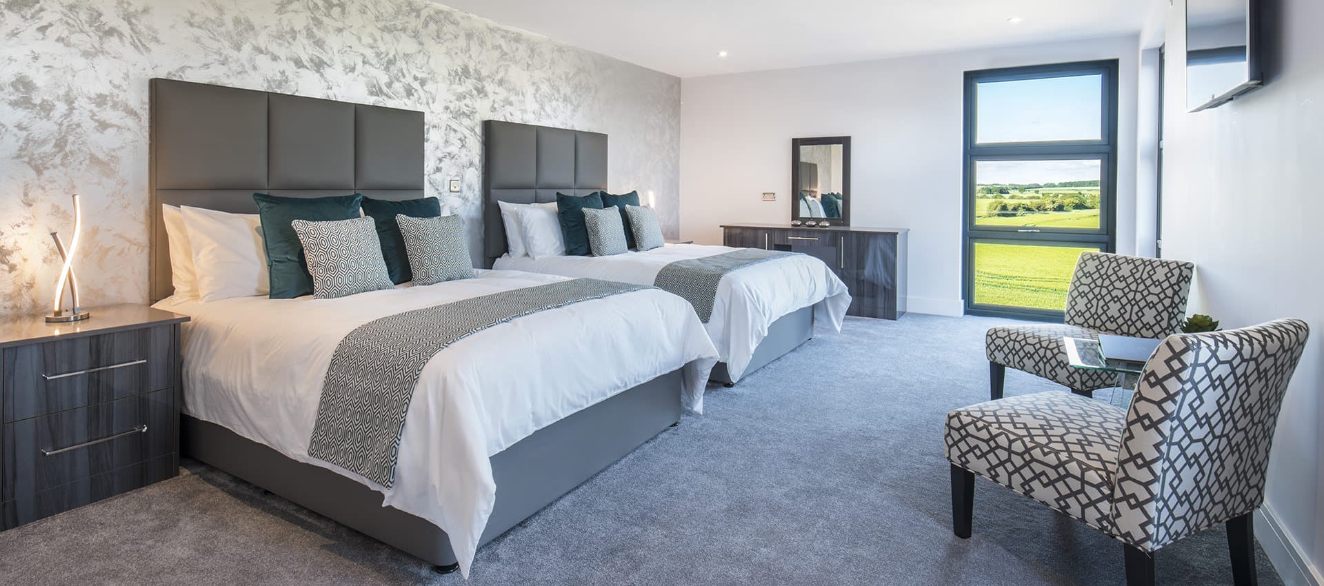 Two beds in room with desk, chairs and window with a view