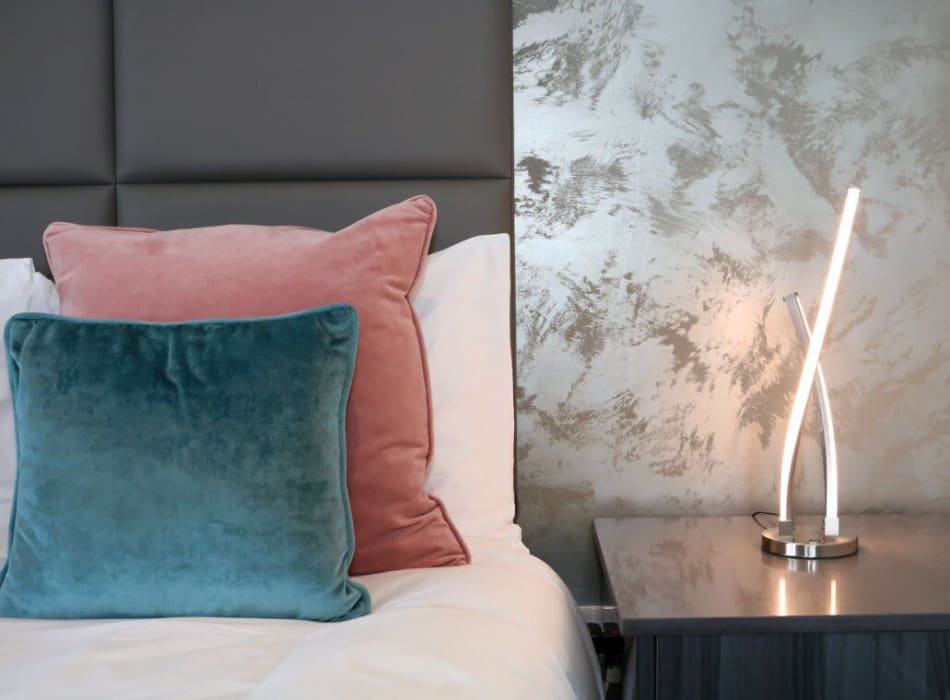 Lamp on bedside table next to cushions on bed